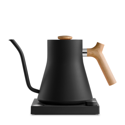 The Stagg EKG Electric Kettle from Fellow Wholesale features a sleek black finish, precise gooseneck spout, wooden handle, and wooden lid knob. Its minimalist design is enhanced by variable temperature control, and it sits elegantly on a black base.