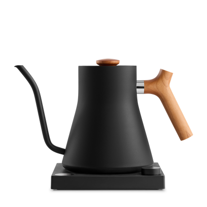 A sleek, matte black Stagg EKG Electric Kettle from Fellow Wholesale, featuring a slender and precise gooseneck spout and adorned with a wooden handle, sits gracefully on its matching black base. The minimalist design showcases a modern aesthetic and includes variable temperature control for achieving the perfect brew.