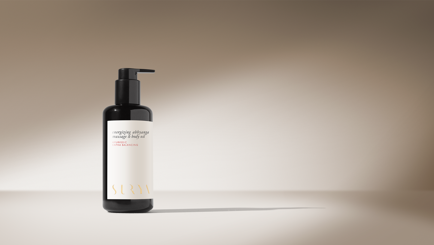 A sleek black bottle with a pump dispenser sits on a light surface against a beige background. The label reads "SURYA" at the bottom, and "Energizing Body Oil" in the middle in elegant font. Minimalist design with soft lighting evokes an Energizing Massage Oil aesthetic.