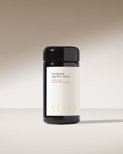 A black cylindrical container labeled "Energizing Digestive Spice Blend" stands against a gradient background transitioning from light to dark beige. The minimalistic label features "Surya" at the bottom, highlighting its commitment to organic ingredients.