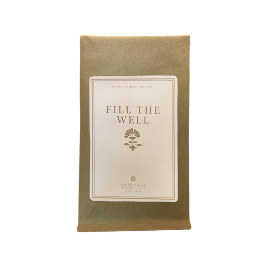 A brown paper package labeled "Fill The Well Herbal Infusion" with a simple floral emblem beneath the text. The label also reads "Nourishing Herbal Infusion," emphasizing self care, and includes the branding "Moon Canyon Healing.