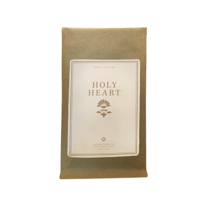 A brown paper pouch with a minimalist and elegant design features a white label at its center. The label prominently displays "Holy Heart Tea Blend" in bold letters, with “Herbal Tea Blend” elegantly printed above it. Below, the small logo reads “Moon Canyon Healing” along with additional text. 