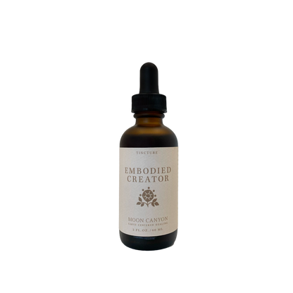 The Embodied Creator Tincture from Moon Canyon Healing comes in a brown glass bottle with a black dropper cap. The label, which features a minimalist design with a small rose icon and specifies the product as a tincture measuring 2 fl. oz. (59 mL), stands out against the black background.