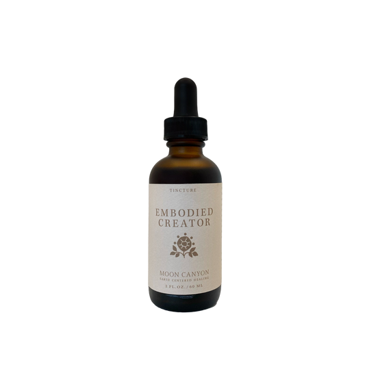 The Embodied Creator Tincture from Moon Canyon Healing comes in a brown glass bottle with a black dropper cap. The label, which features a minimalist design with a small rose icon and specifies the product as a tincture measuring 2 fl. oz. (59 mL), stands out against the black background.