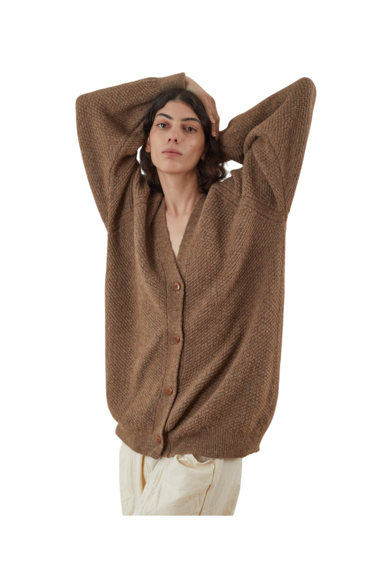 Clad in the Wol Hide Moss Cardigan in Earth, a person with an oversized fit and buttoned front layers it over cream pants, lifting their arms to rest behind their head against a plain white background.