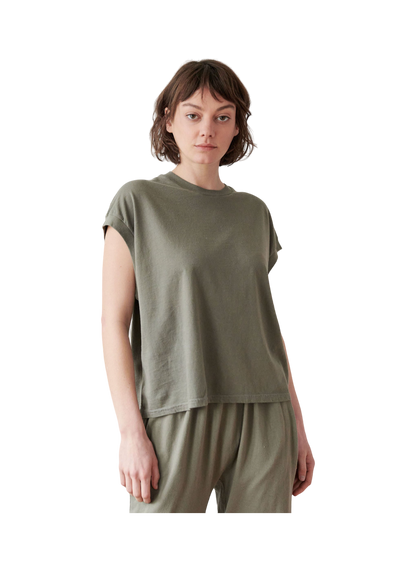 A person stands facing forward wearing the Cotton Jersey Box Tee in Fir from Wol Hide, paired with matching pants. The individual has short brown hair and a neutral expression, set against a plain background that remains out of view.