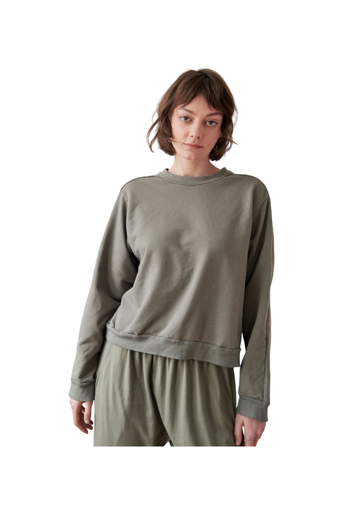 A person with short, brown hair is wearing a loose-fitting, long-sleeved Cotton French Terry Easy Summer Sweatshirt in Fir by Wol Hide and matching pants. They are standing against a plain background, gazing forward with a neutral expression.