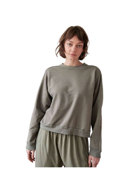 A person with short, brown hair is wearing a loose-fitting, long-sleeved Cotton French Terry Easy Summer Sweatshirt in Fir by Wol Hide and matching pants. They are standing against a plain background, gazing forward with a neutral expression.