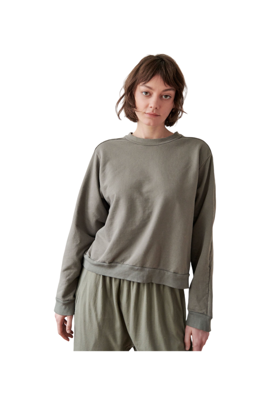 A person with short, brown hair is wearing a loose-fitting, long-sleeved Cotton French Terry Easy Summer Sweatshirt in Fir by Wol Hide and matching pants. They are standing against a plain background, gazing forward with a neutral expression.