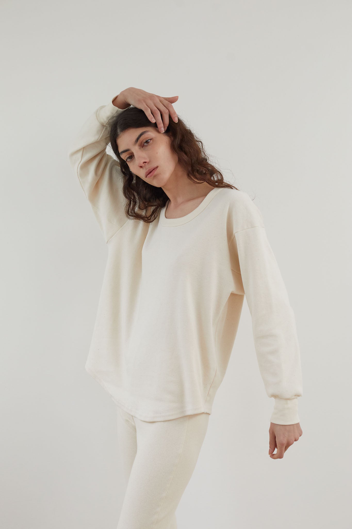 An individual clad in a Wol Hide Scoop Neck Thermal in Natural along with matching pants, striking a pose with one arm bent above their head and the other resting on their hip, set against a plain backdrop.