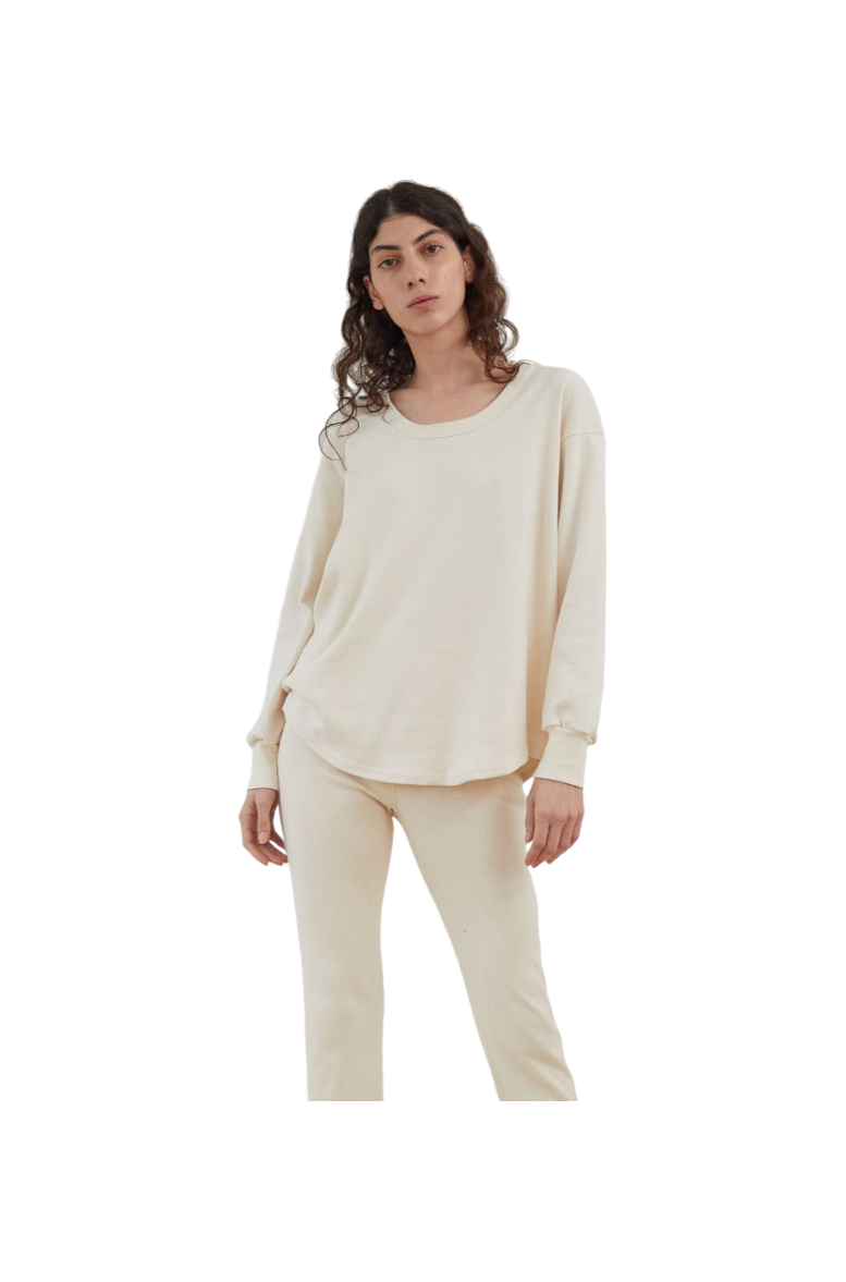 A person with long, curly hair is wearing Wol Hide's Scoop Neck Thermal in Natural, paired with matching pants, standing against a plain white background.