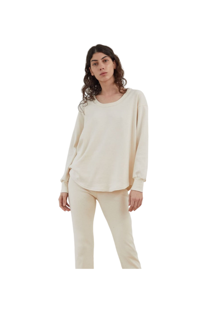 A person with long, curly hair is wearing Wol Hide's Scoop Neck Thermal in Natural, paired with matching pants, standing against a plain white background.