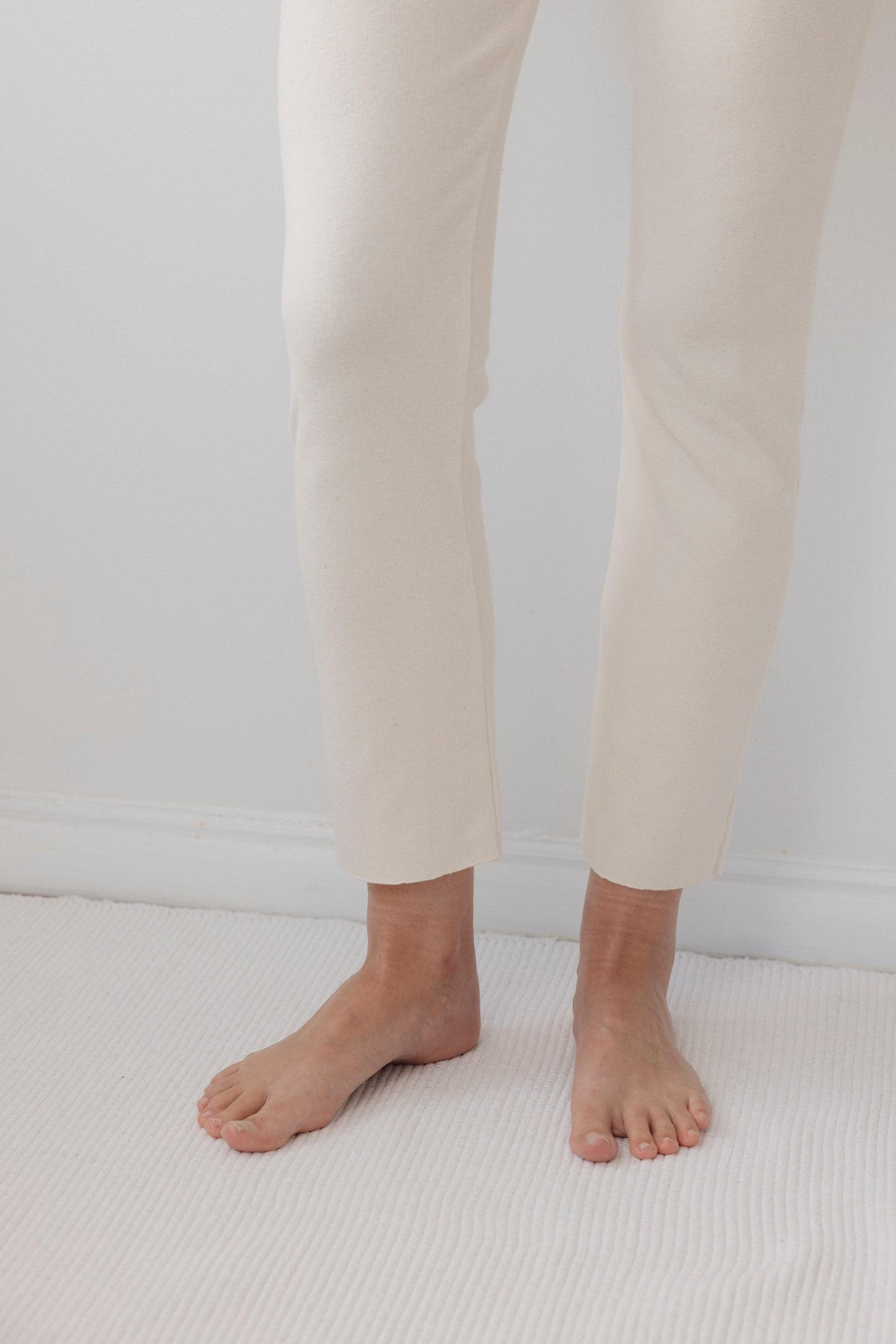 A person standing barefoot on a white carpet, wearing Wol Hide's Easy Legging in Natural, with a plain white wall as the background.