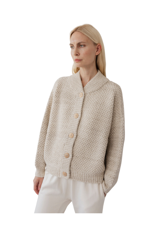 A person with light blonde hair wears the Wol Hide Box Bomber in Chalk, featuring a textured, undyed marled effect and large buttons. Paired with white pants, they gaze to the side against a plain black background.