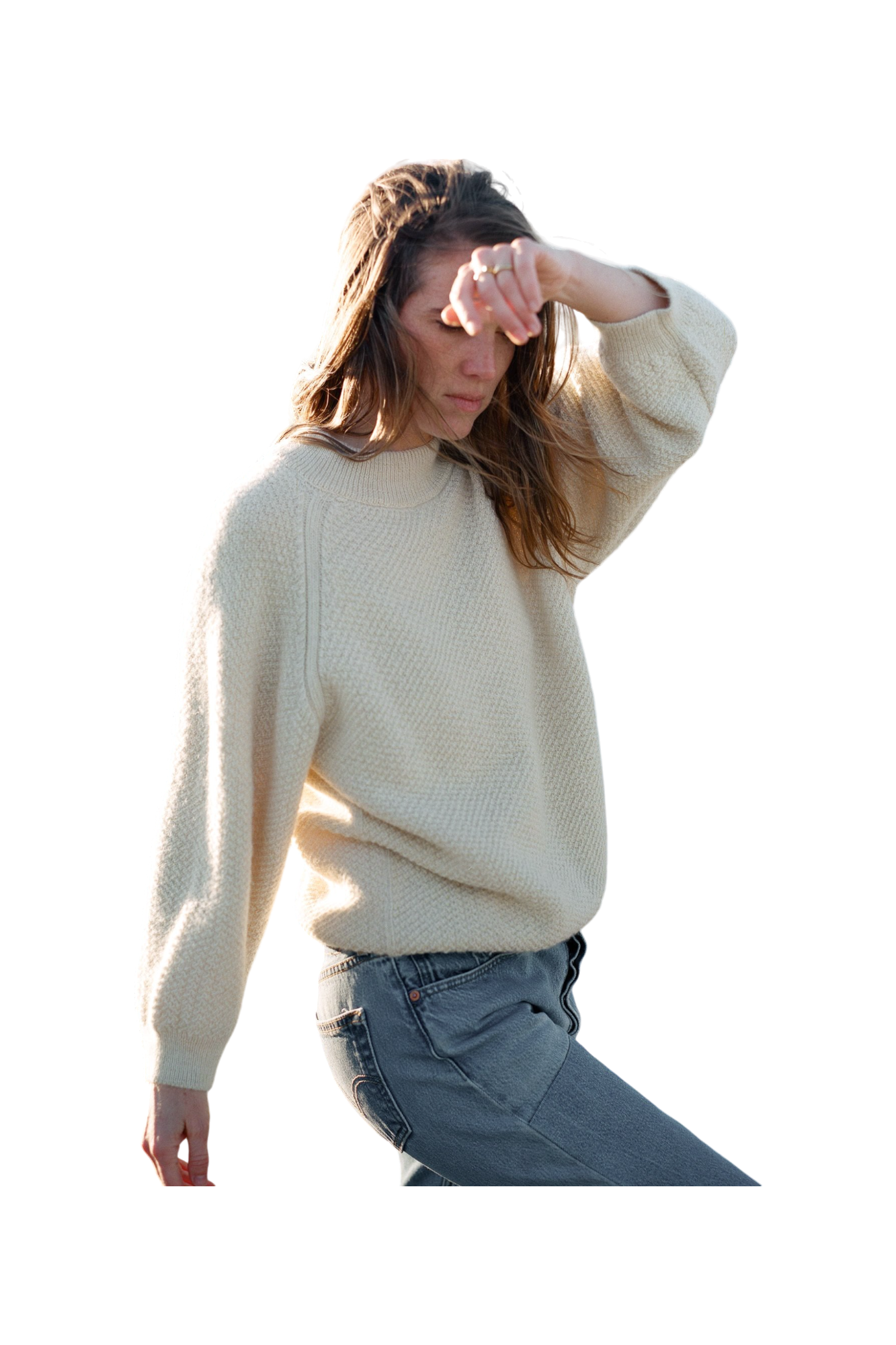 A person with long hair, dressed in a Wol Hide Wool and Alpaca Blend Sweatshirt Sweater in Natural and jeans, is captured mid-motion with one arm raised and the other relaxed by their side. 