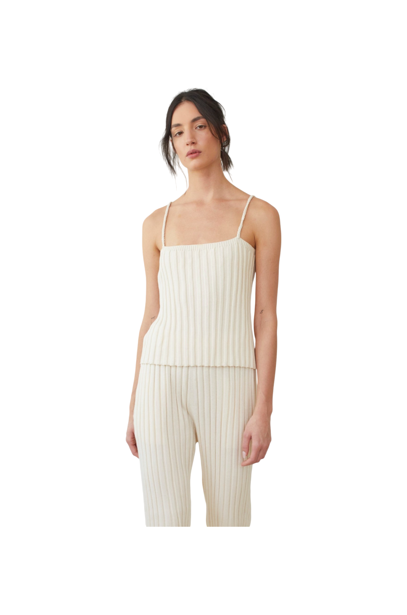 A person wearing the Rib Cami in ecru by Wol Hide, featuring a cream-colored, wide rib stitch design with braided straps, and matching pants. They have dark hair tied back and are standing against a plain white background.