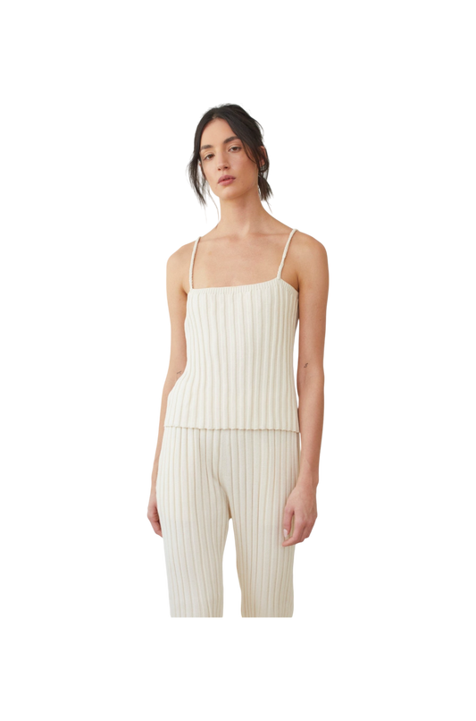 A person wearing the Rib Cami in ecru by Wol Hide, featuring a cream-colored, wide rib stitch design with braided straps, and matching pants. They have dark hair tied back and are standing against a plain white background.