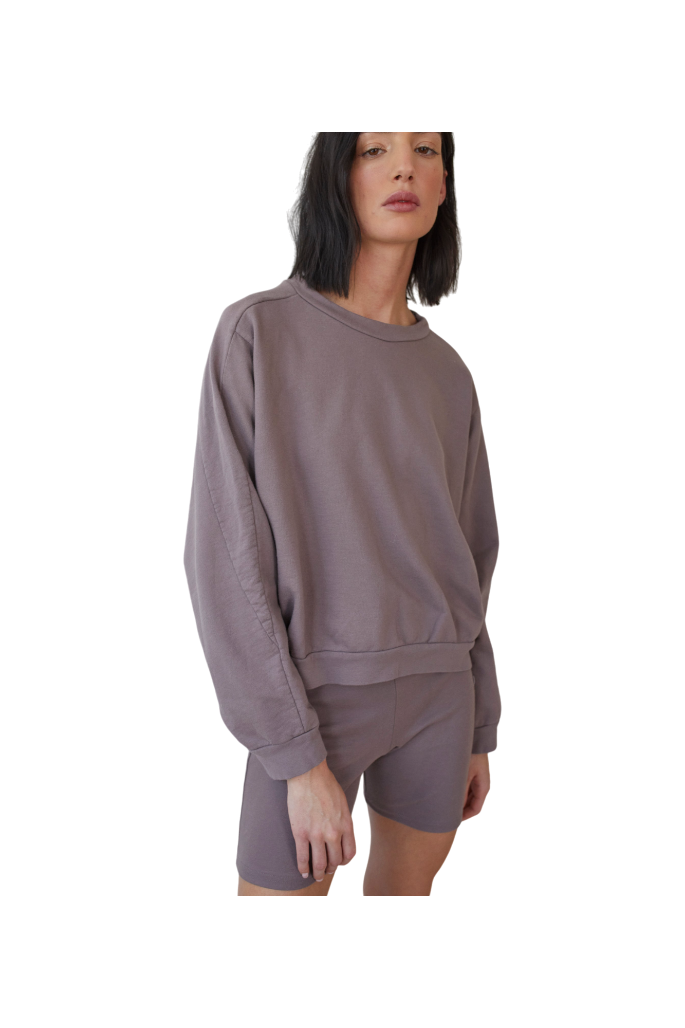 A person with shoulder-length dark hair is wearing an oversized, long-sleeve, Wol Hide Cotton French Terry Easy Summer Sweatshirt in Mushroom, paired with matching shorts. They have a serious expression and are posing against a plain, white background. Made in USA.