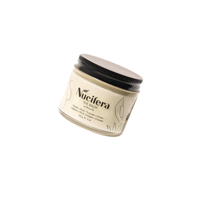 A beige jar of "The Balm" from Nucifera Body Store's The Essentials Kit, complete with a black lid, set against a black background. The label showcases the brand name and product details, enhanced by minimalist leaf illustrations. The jar is tilted, highlighting the versatile skincare packaging design.