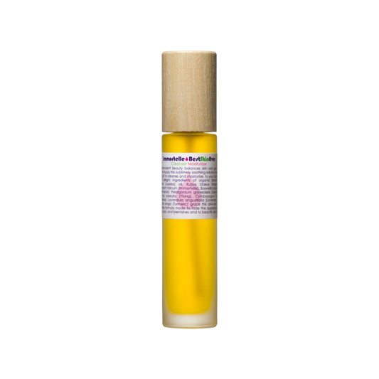 A small glass roll-on bottle filled with yellow liquid, labeled "Best Skin Ever Cleanser - Immortelle" by Living Libations, offers complexion perfection. The bottle, capped with wood, hints at a luxurious oil or serum ideal for those with skin sensitivities. Set against a plain white background, it promises gentle and effective skincare.