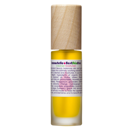 A glass bottle filled with yellow liquid, featuring a wooden cap and a label reading "Best Skin Ever Cleanser- Immortelle" by Living Libations. The label lists ingredients and product descriptions, indicating that it is a cleanser and moisturizer designed for facial skin care, promoting complexion perfection especially for sensitive skin.