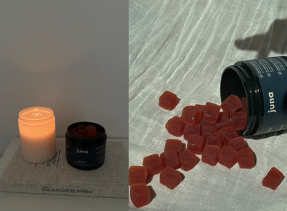 A dimly lit candle next to an open container labeled "Juna Nightcap Sleep Gummies" containing square-shaped sleep aid gummies sits on top of a book titled "The Five Minute Journal." Beside it, another view shows the container with numerous functional botanical gummies spilled out onto a fabric surface.