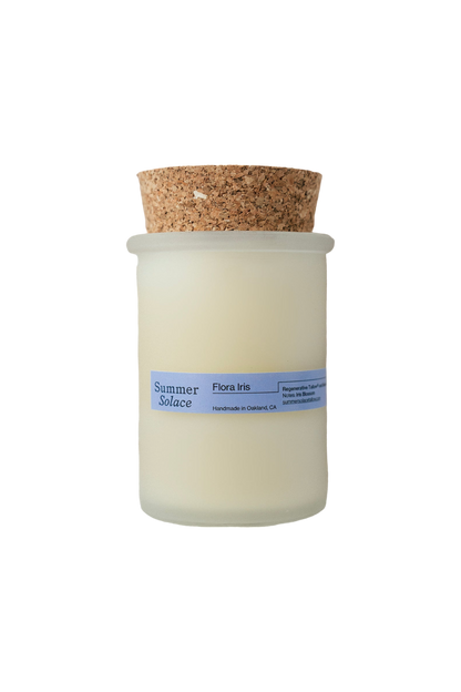 A frosted glass jar candle with a cork lid, featuring a light blue label that reads "Summer Solace Tallow" and "Flora Iris Candle - Regenerative Tallow™." It is handmade in Oakland, CA. The cream-colored wax ensures the sustainable tallow candles feel luxurious.