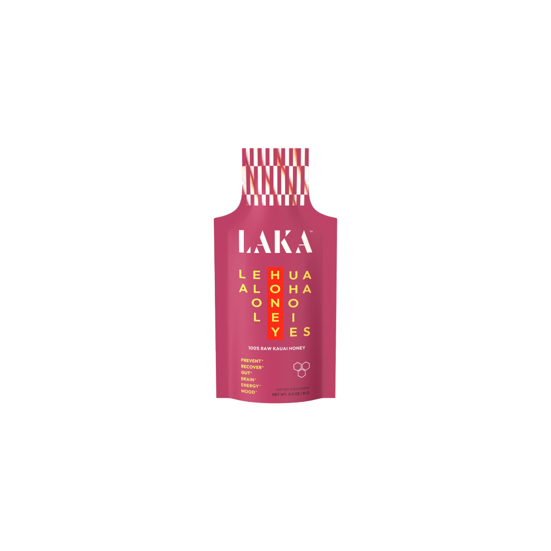 A pink packet labeled "LAKA" in white, featuring a yellow grid with the words "LEHUA HONEY ALOHA" displayed both horizontally and vertically. The text at the bottom states "100% RAW KAUAI HONEY," indicating it provides immune support with no added sugars or dairy, and promotes sweet energy. The cap is red and white striped. This product is known as LAKA Honey Sticks™ by the brand LAKA.
