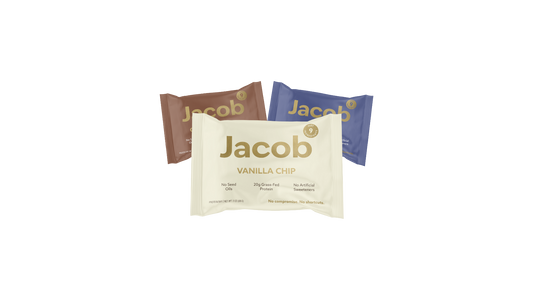 Three Jacob Bar snack packages are displayed. The front package is Vanilla Chip in beige, while behind it are two other packages: one in brown and another in dark blue, with indistinct flavor labels. Made with 100% Organic Cacao, these bars contain no seed oils, soy, or artificial sweeteners.