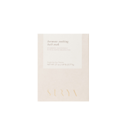 A minimalist beige package of Surya Hormone Soothing Bath Soak, labeled as tridoshic and balancing Pitta & Kapha. The packaging features gold text for the product name and weight details, which include 27 oz, 1.69 lb, and 0.77 kg. Infused with Shatavari, the brand name "Surya" is embossed.