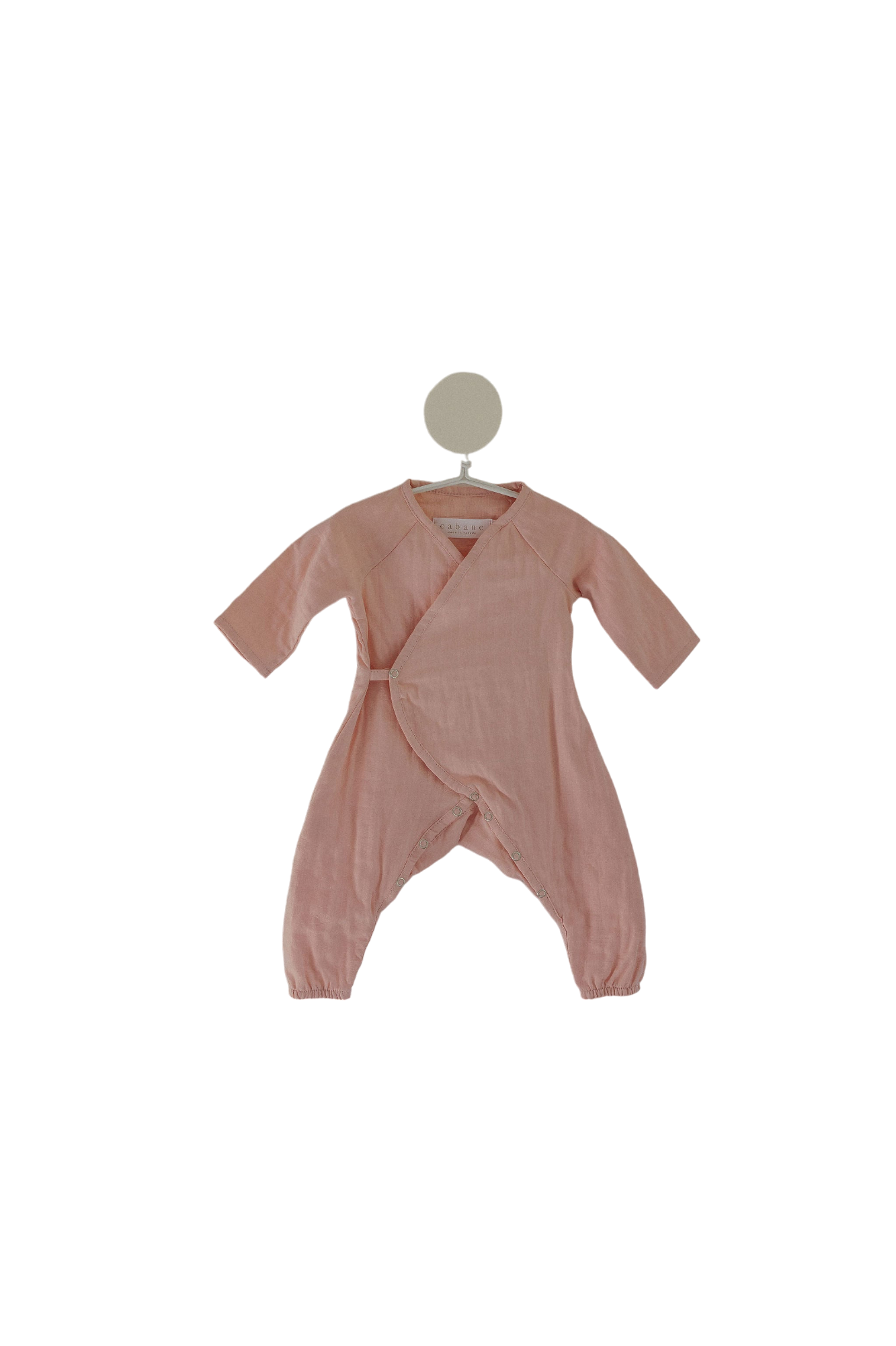 The Après Wrap in Desert Rose by cabane childrenswear is displayed on a white hanger. This ethically handmade, long-sleeved baby romper features a criss-cross front design and enclosed feet. Made from organic cotton double gauze wrap, it is soft and comfortable, perfect for infants with sensitive skin.