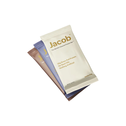 Three bars from Jacob Bar, each labeled "The Jacob Bar," are stacked. The top bar features a vanilla chip flavor and contains 20g of grass-fed whey protein, free of seed oils and artificial ingredients. The bars below are wrapped in various colors, each meticulously crafted to perfection without compromising on taste or quality.