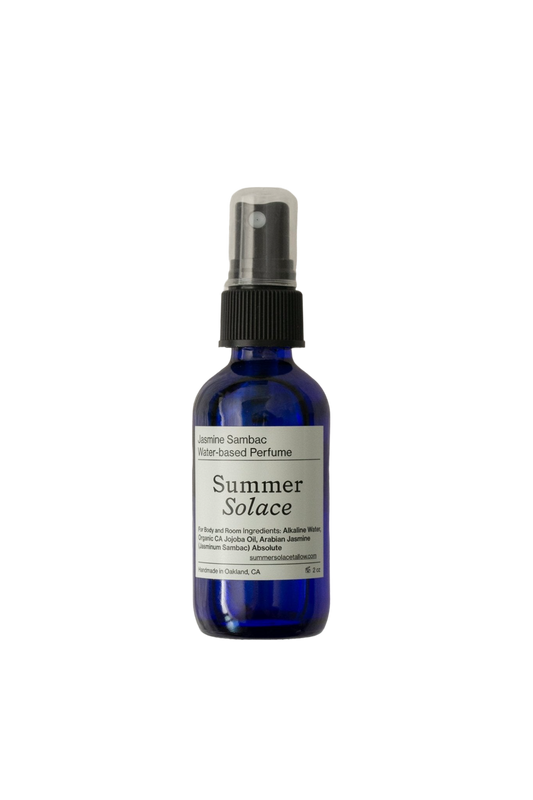 A cobalt blue spray bottle of "Summer Solace Tallow" Jasmine Sambac (with Rose Ormus) Water-Based Perfume Mist, featuring jasmine sambac and magnolia absolute, has a black cap and a white label detailing the product, including ingredients like organic witch hazel and essential oils.