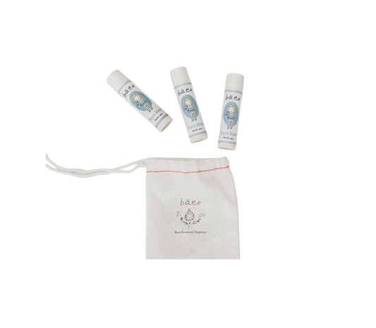 The image features three small bottles with blue and white labels and white caps, containing baby skincare products from "bāeo." Below the bottles is a white drawstring pouch with the "bāeo" logo and the text "Bāeo Essential Organics" printed on it. Also included is their organic lip balm, named "bare kiss," in a plant-based tube.