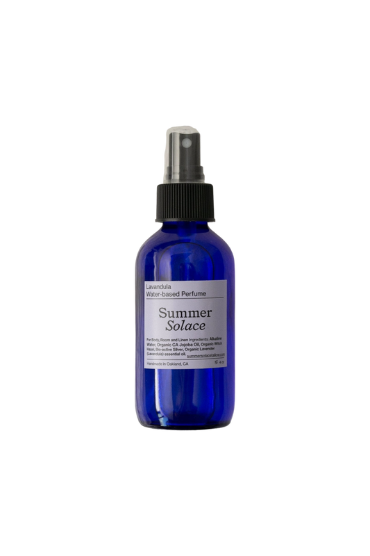 A blue glass bottle with a spray nozzle labeled "Lavandula (with Lotus Ormus) Water-Based Toner Mist" and "Summer Solace Tallow," featuring organic Bulgarian lavender. The label also includes comprehensive details about the product and company. The bottle is set against a plain black background.