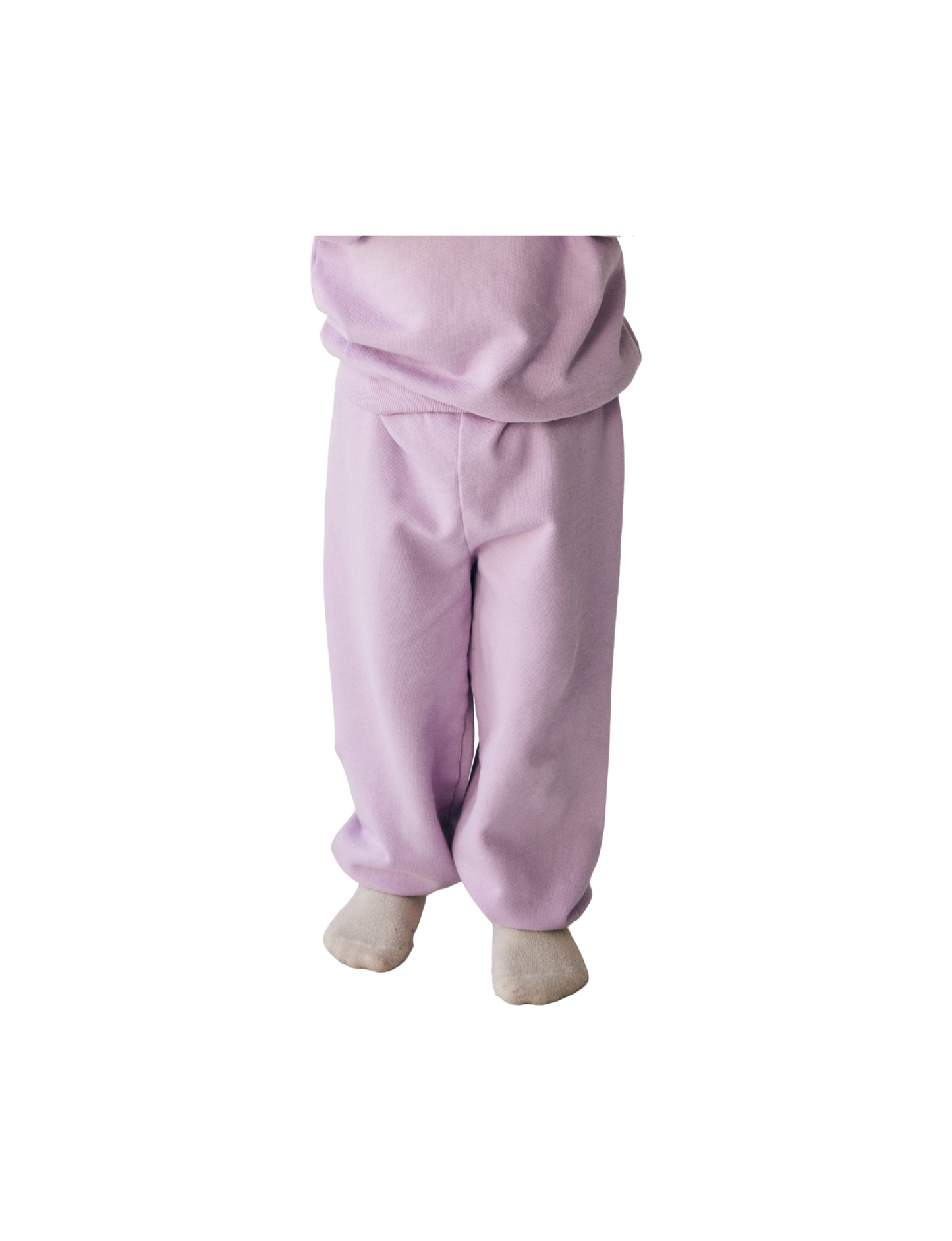 A partial view of a child standing, showing from the shoulders down, dressed in "The Lil' Classic Sweatpant" from all the babies. The cozy outfit features light purple organic French terry cloth pants and a matching top, with only the feet in white socks visible. The background is transparent.