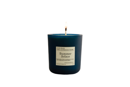 A blue candle in a glass container is lit, with the flame burning brightly at the top. The label reads, "Vanilla Nectar + Peru Balsam Tallow and Beeswax Candle 8 oz. - Summer Solace Tallow". The background is completely black, highlighting the clean-burning vanilla candle's warm glow.