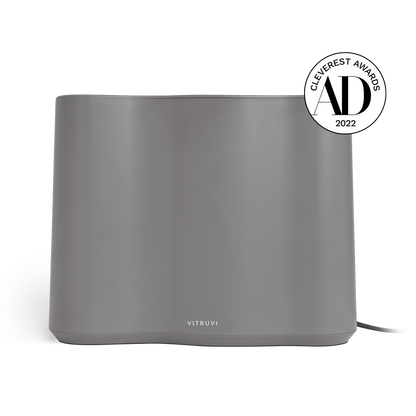 A sleek, gray Vitruvi Cloud Humidifier with a minimalist design, featuring the brand name "Vitruvi" on the front. Incorporating ultrasonic technology for enhanced performance, it has been awarded the 'Cleverest Awards 2022' by AD, as indicated by the badge displayed on the upper right corner.