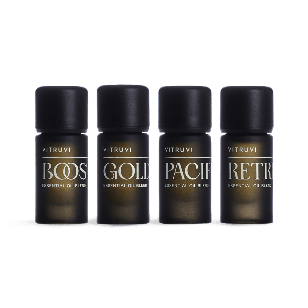 The Vitruvi Refresh Diffuser Blend Kit showcases four small, dark bottles of revitalizing essential oil blends, neatly lined up. Each bottle is labeled with the names "BOOST," "GOLD," "PACIFIC," and "RETREAT." With black caps set against a white background, these oils are designed to invigorate your atmosphere.