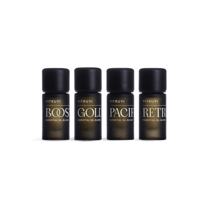 Four dark brown glass bottles with black caps feature a variety of essential oil blends by Vitruvi. The labels read: BOOST, GOLD, PACIF, and RETR. This non-toxic Refresh Essential Oil Kit is perfect for creating a serene environment. The white background highlights the beautifully designed Vitruvi products.