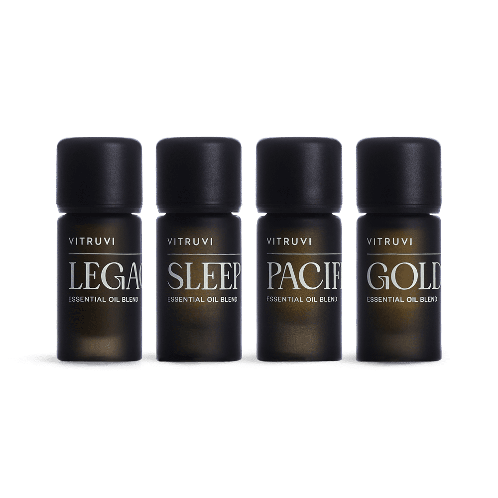 The Signature Diffuser Blend Kit from Vitruvi, featuring four essential oil blends named Legacy, Sleep, Pacific, and Golden, is elegantly displayed. With minimalist packaging that sports black caps and white lettering, these premium scents are designed to cultivate a harmonious ambiance in any space.