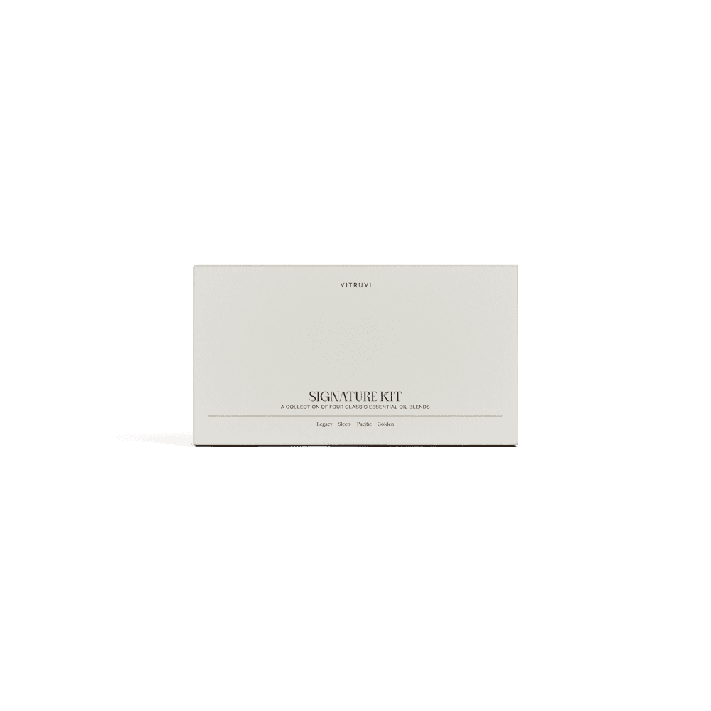 A minimalist white box featuring the brand name "Vitruvi" and the product name "Signature Diffuser Blend Kit" is accompanied by a subtitle highlighting its role as a collection of essential oil blends for relaxation and stress relief. The clean design includes a shadow beneath the box, all set against a solid green background.