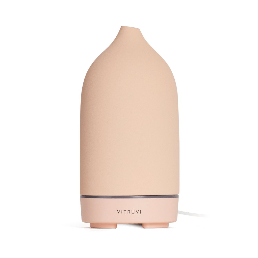 The Vitruvi Stone Diffuser is a beige ceramic diffuser with a smooth, conical shape and a simple, sleek design. It features the "Vitruvi" branding on the front and complements any home decor. Set against a plain white background, it's perfect for diffusing pure essential oils.