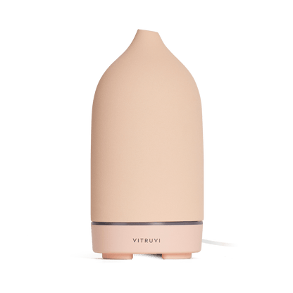 The Vitruvi Stone Diffuser is a beige ceramic diffuser with a smooth, conical shape and a simple, sleek design. It features the "Vitruvi" branding on the front and complements any home decor. Set against a plain white background, it's perfect for diffusing pure essential oils.