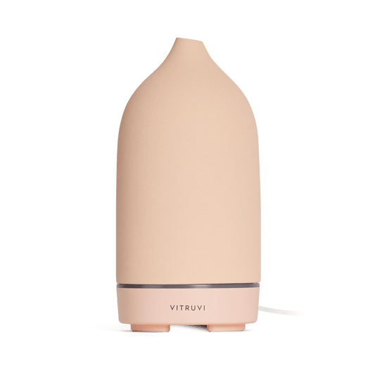 The Vitruvi Stone Diffuser is a beige ceramic diffuser with a smooth, conical shape and a simple, sleek design. It features the "Vitruvi" branding on the front and complements any home decor. Set against a plain white background, it's perfect for diffusing pure essential oils.