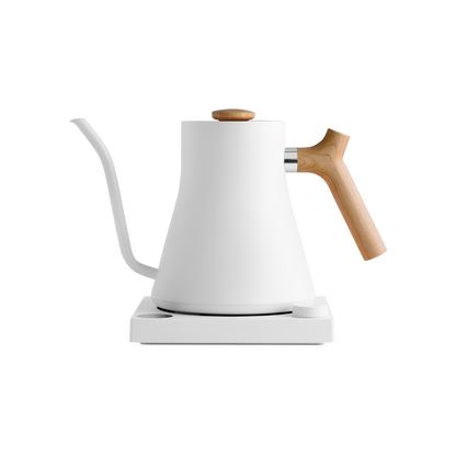 A modern white Fellow Wholesale Stagg EKG Electric Kettle with a matte finish is placed on a matching white base. It features a gooseneck spout and light wooden handle and lid knob. The sleek design combines variable temperature control with aesthetics, making it ideal for precision pouring in pour-over coffee.
