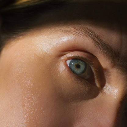 Close-up of a person's eye with a blue iris, partially covered in shadow. The image focuses on the eye and surrounding skin, capturing fine details of the texture and light—much like the refined results achieved with Emanations Nourishing Face and Hair Oil-Animal-based from Summer Solace Tallow. The eyelashes and a portion of the eyebrow are also visible.