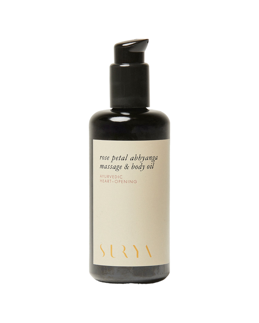 A bottle of Rose Petal Body Oil from the brand Surya, featuring a pump dispenser. The cream-colored label with gold lettering reads "Ayurvedic Heart-Opening." Handmade by Martha, the sleek black bottle captures the essence of rose essential oil.