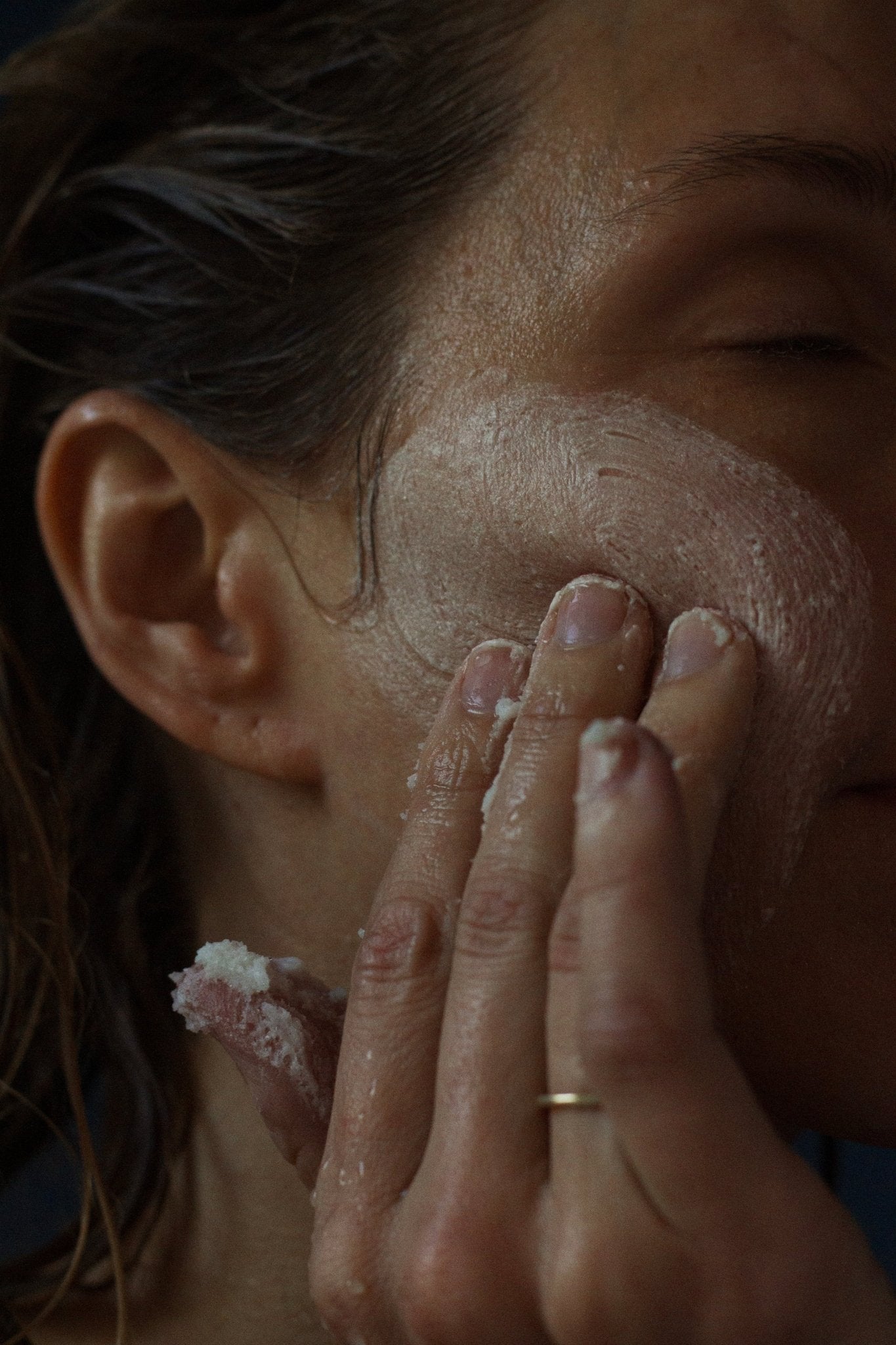 A person applies the SEELE Celtic Sea Salt® Scrub - Regenerative Tallow® by Summer Solace Tallow to their cheek using their fingertips. The skin appears moist, and the person has their eyes closed. The focus is on the hand and face, emphasizing the texture of the scrub infused with Celtic Sea Salt®.