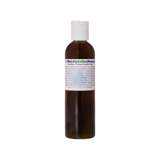 A small brown bottle with a white cap, labeled "True Blue Spirulina Shampoo" from Living Libations. The label also features text about revitalizing and renewing healthy, colored hair with azulene-containing essential oils and a list of botanical ingredients including spirulina, aloe barbadensis, and various extracts.